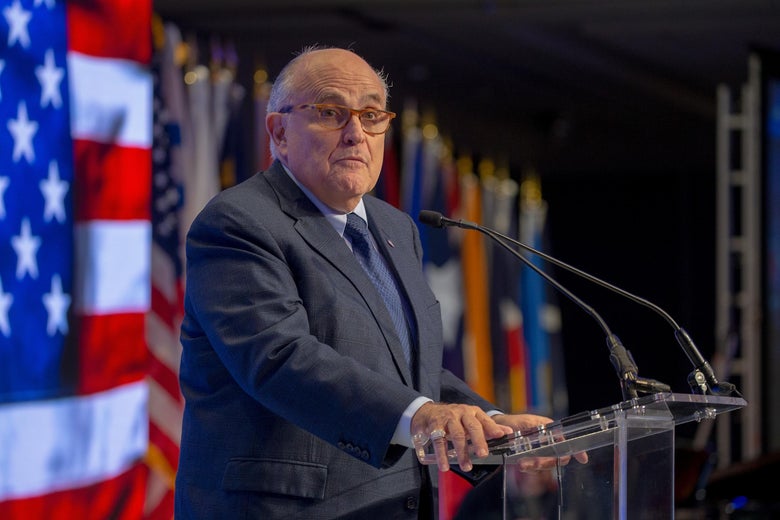 Rudy Giuliani stands at a glass podium.